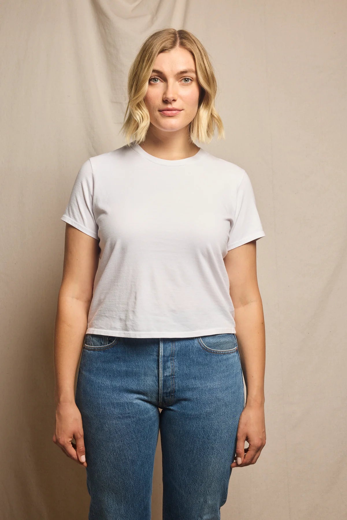 Woman wearing a plain white t-shirt and blue jeans against a beige background, size L