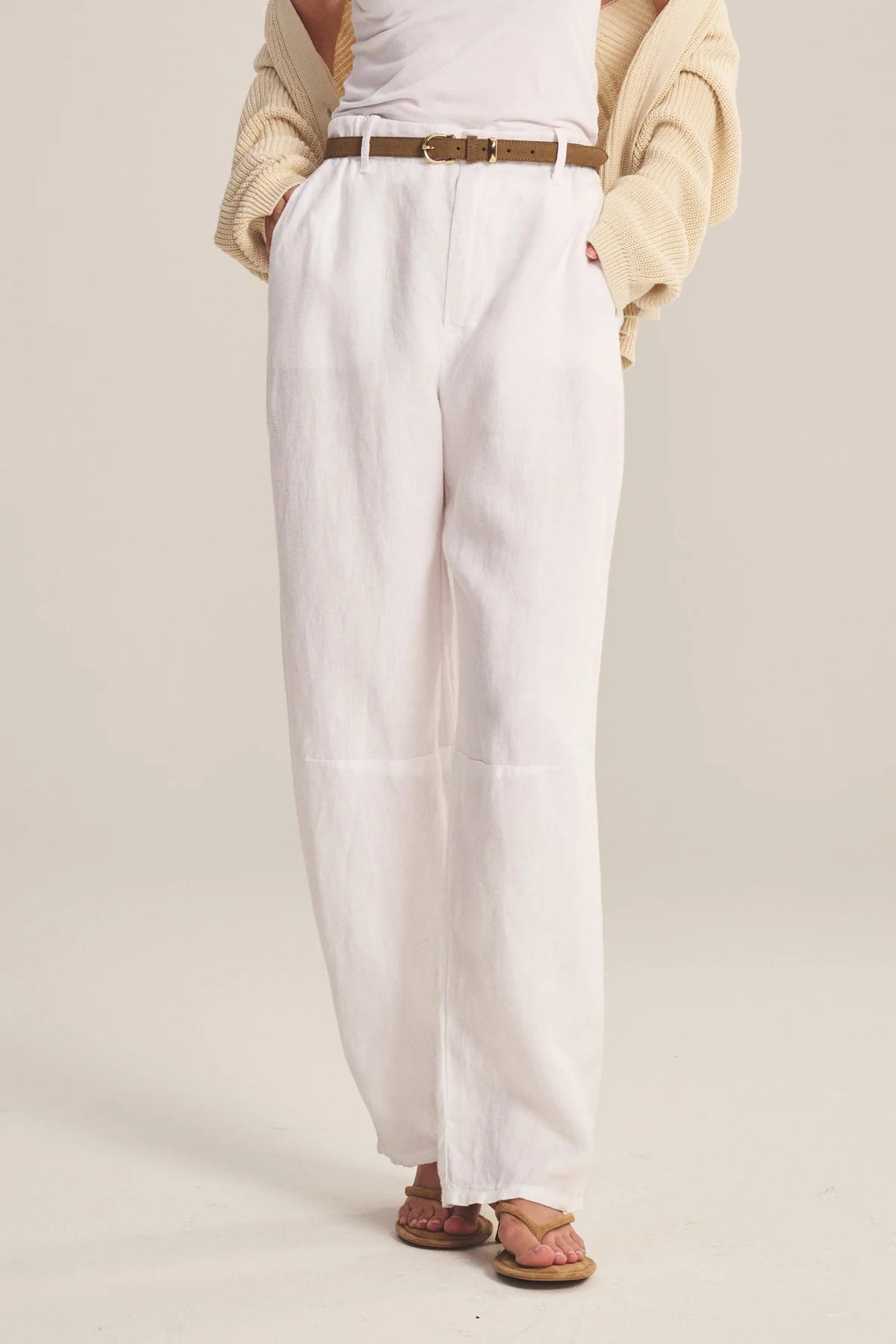 Person wearing white pants with a beige sweater on a plain background