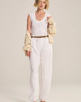 Woman wearing a white sleeveless top and pants with a beige cardigan on a plain background