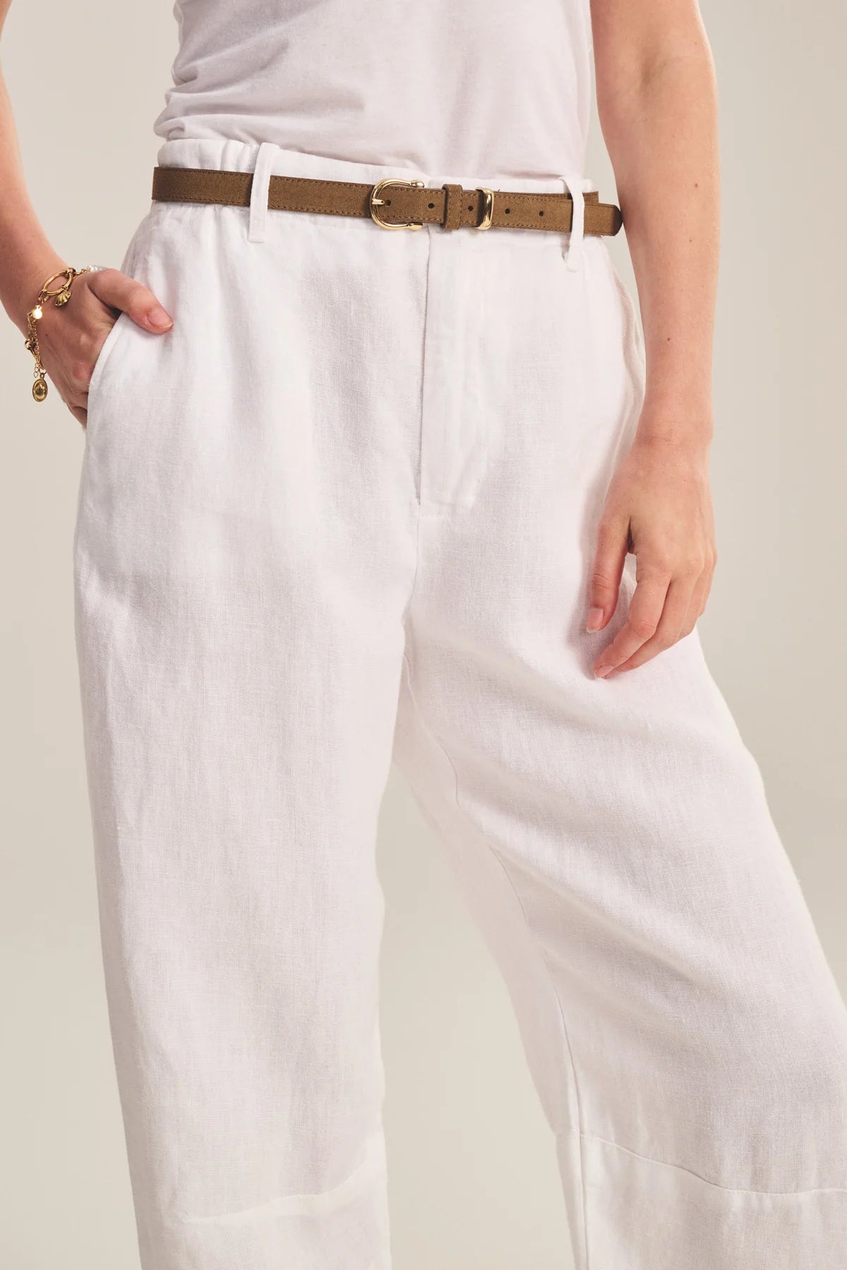 Person wearing white pants with a brown belt on a neutral background