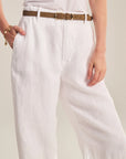 Person wearing white pants with a brown belt on a neutral background