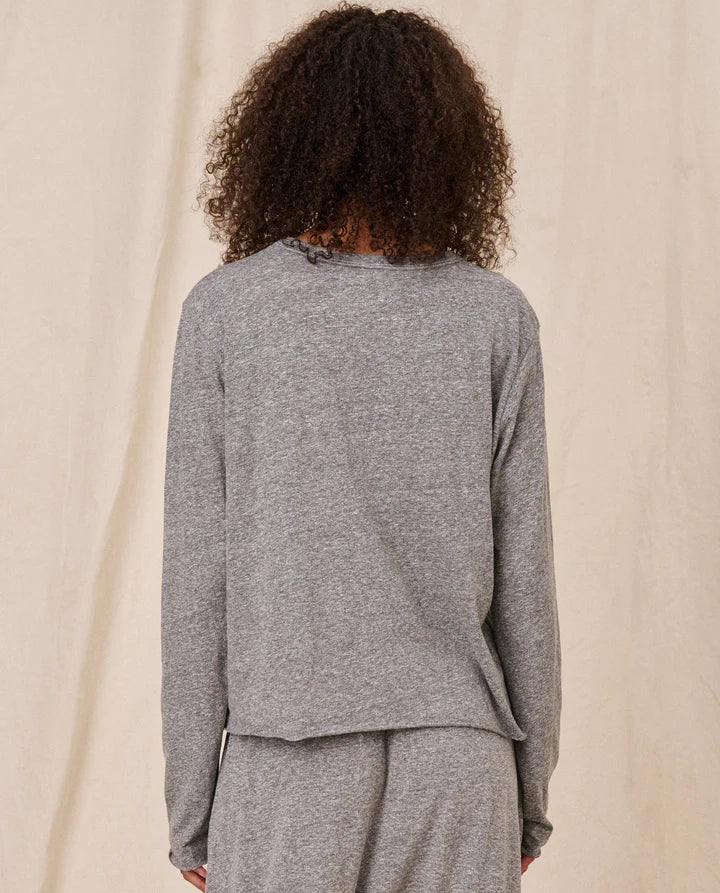 Person wearing a gray long-sleeve top and pants against a beige background, back