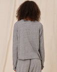 Person wearing a gray long-sleeve top and pants against a beige background, back