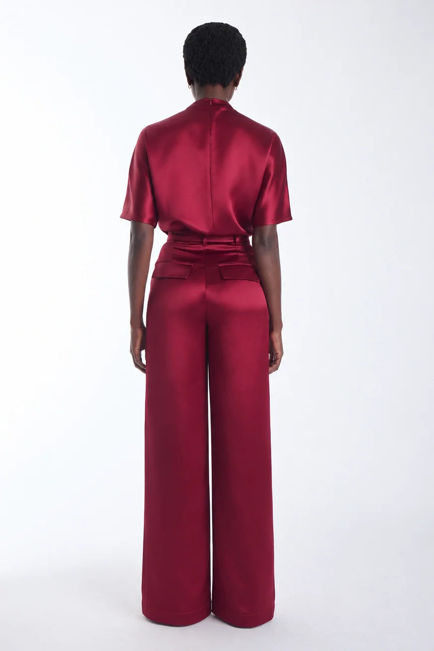 A model viewed from the back wearing a deep burgundy short sleeves top with a high collar, and wide leg pants, set against a plain white studio background.