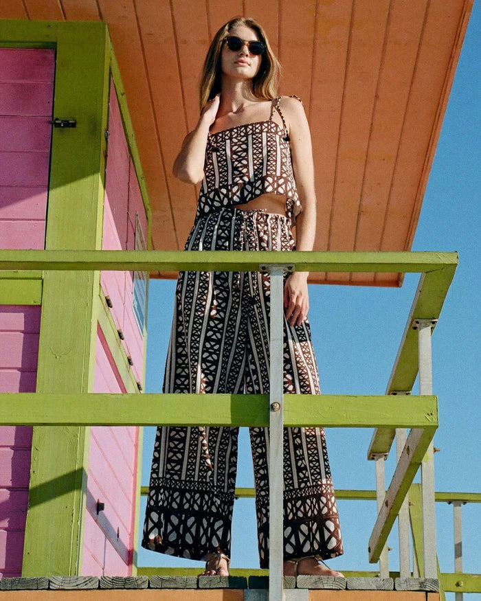 Woman in a patterned set standing on a colorful wooden structure with a clear blue sky.