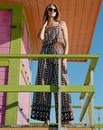 Woman in a patterned set standing on a colorful wooden structure with a clear blue sky.