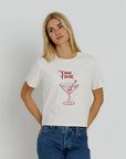 A woman wearing a white short-sleeve graphic t-shirt with a red 'TINI TIME' martini glass illustration on the front, paired with blue jeans, against a light gray studio background.