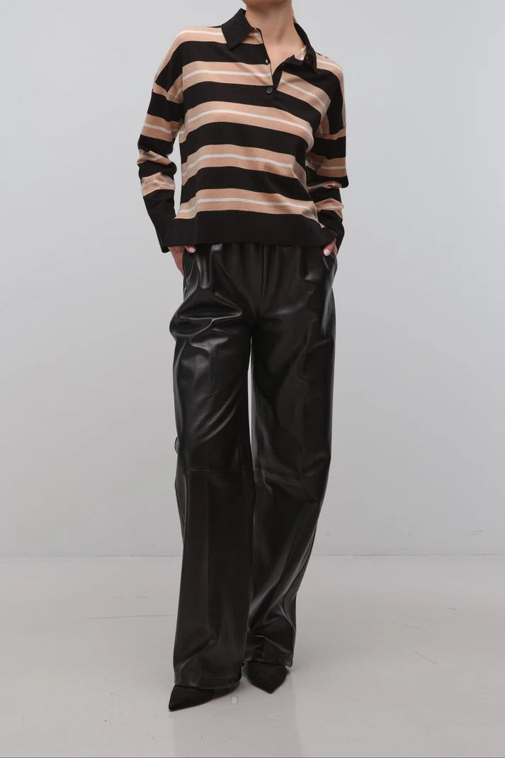 A model wearing a black and beige striped long-sleeve knit polo sweater paired with black wide-leg faux leather pants, standing against a light gray studio background.
