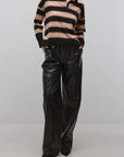 A model wearing a black and beige striped long-sleeve knit polo sweater paired with black wide-leg faux leather pants, standing against a light gray studio background.