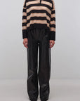 A model stands against a light gray studio background wearing a black and beige horizontally striped knit polo sweater with black wide-leg pants.