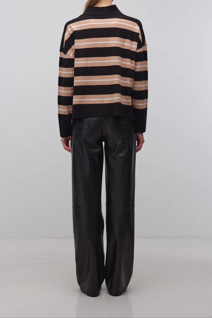 A model viewed from the back wearing a black and beige horizontally striped knit sweater and black wide-leg trousers, standing against a plain light gray studio background.