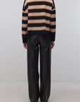 A model viewed from the back wearing a black and beige horizontally striped knit sweater and black wide-leg trousers, standing against a plain light gray studio background.
