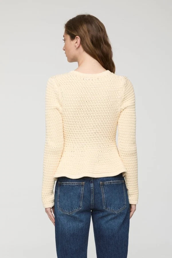 A woman shown from the back wearing a cream-colored textured knit sweater and blue jeans against a light gray studio background.
