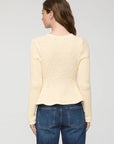 A woman shown from the back wearing a cream-colored textured knit sweater and blue jeans against a light gray studio background.