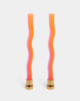 Two wavy candles with pink and orange colors and gold bases on a white background