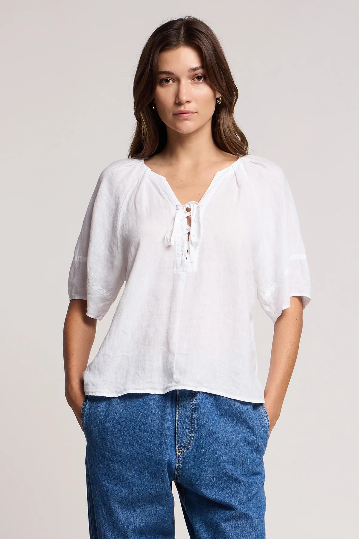 Woman wearing a white blouse and blue jeans against a plain background