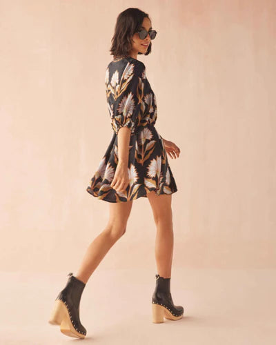 Woman wearing a patterned dress and black boots on a beige background