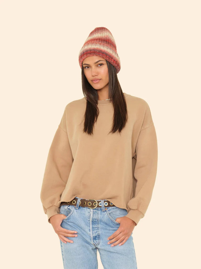 Woman wearing a beige sweater, striped beanie, and blue jeans on a beige background