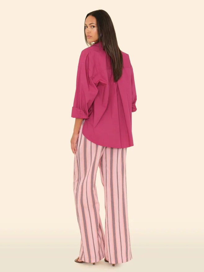 Woman wearing a pink top and striped pants on a beige background back view