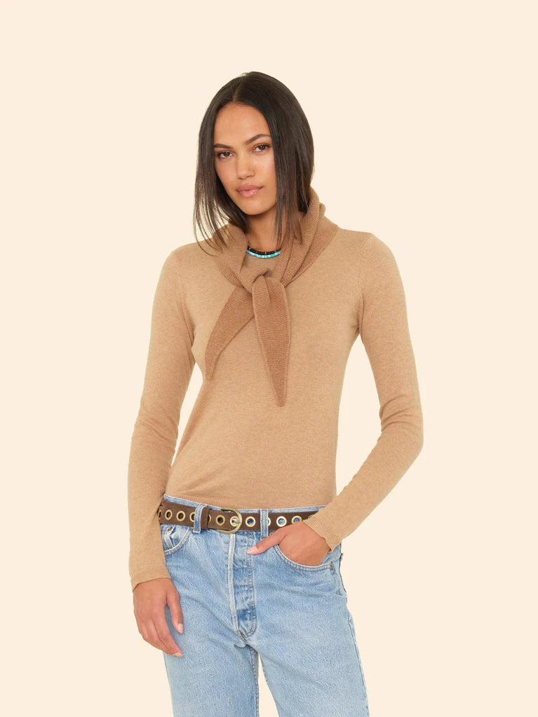 Woman wearing a beige sweater with a scarf and blue jeans on a beige background