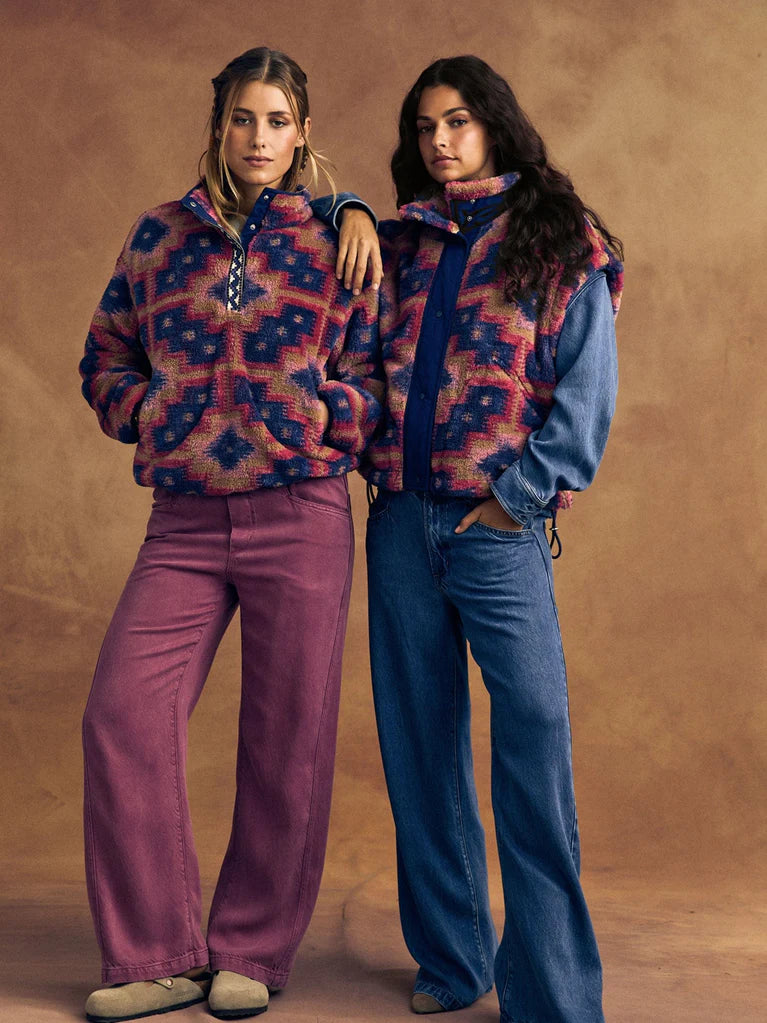 Two women wearing patterned outfits against a brown background
