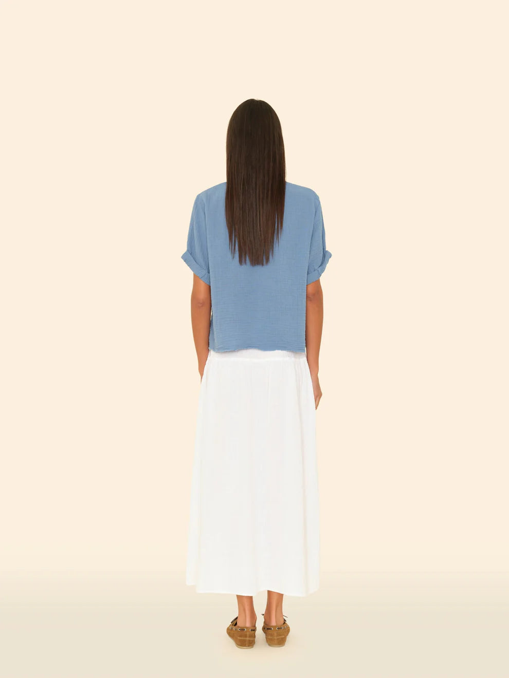 Woman wearing a blue top and white skirt on a beige background