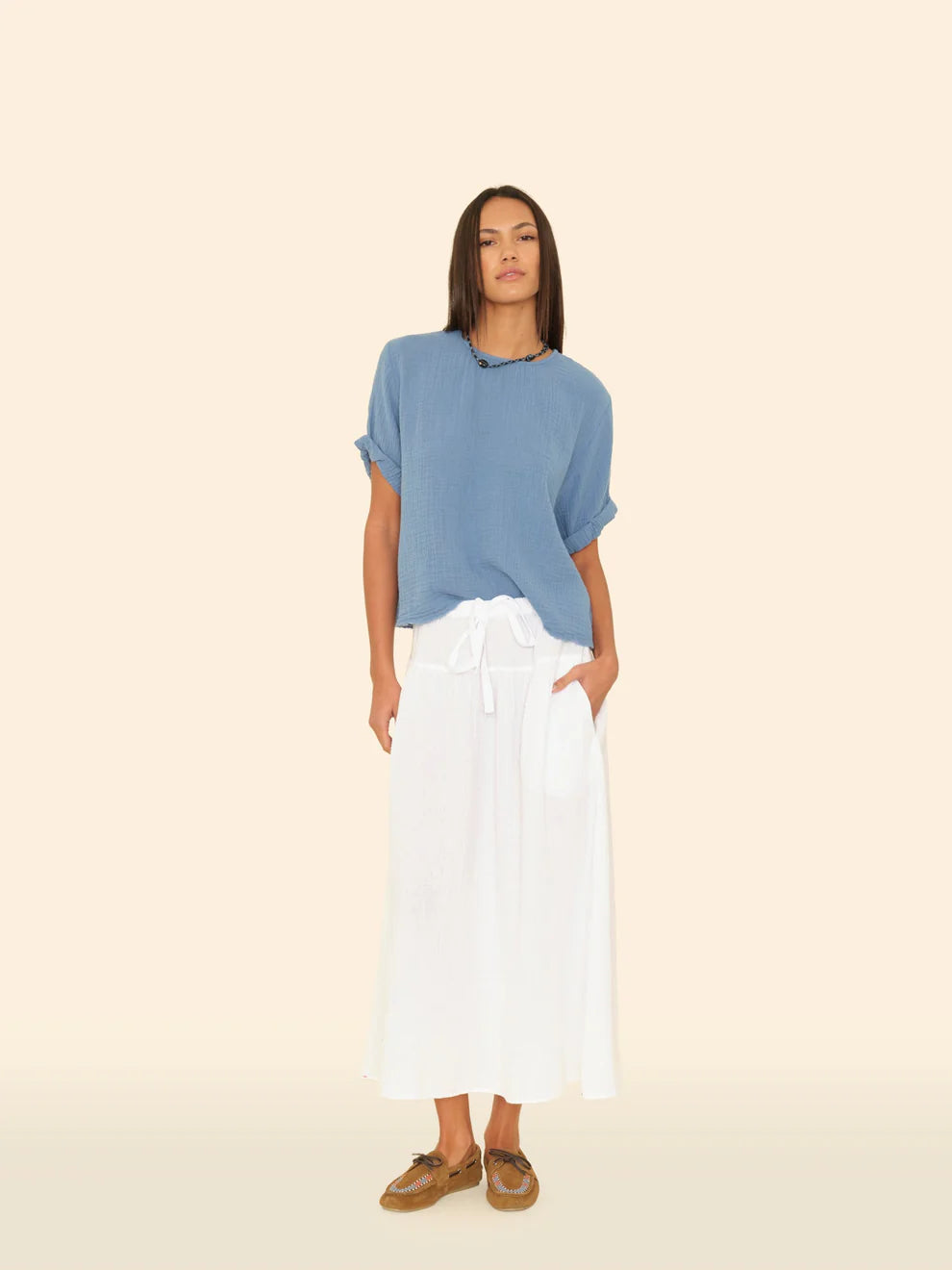 Woman wearing a blue top and white pants on a beige background