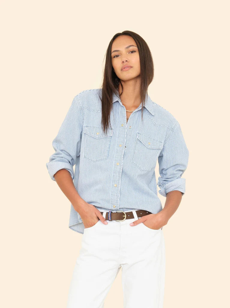 Woman wearing a light blue checkered shirt and white pants on a beige background