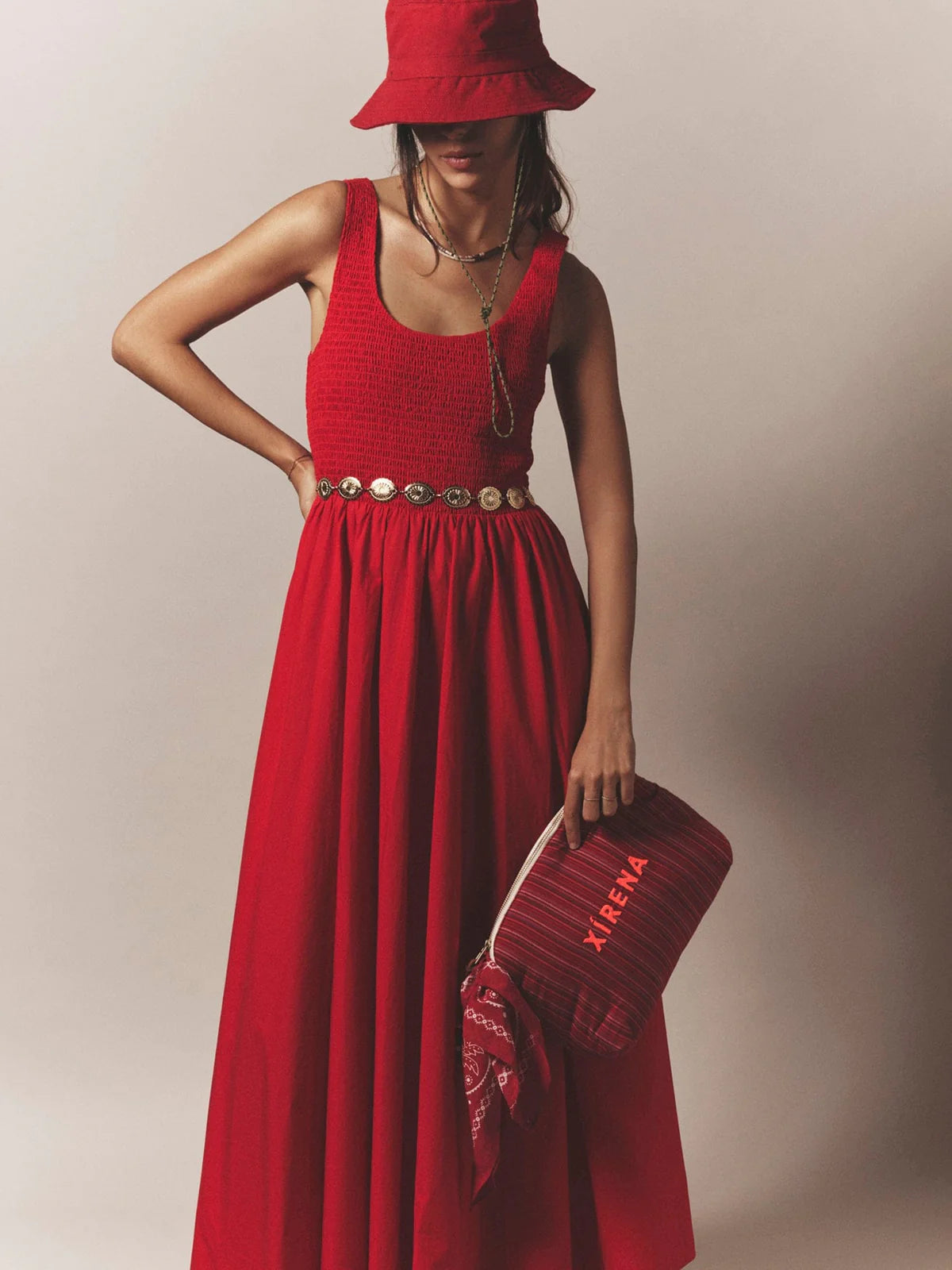 Woman wearing a red dress and hat, holding a matching handbag against a neutral background