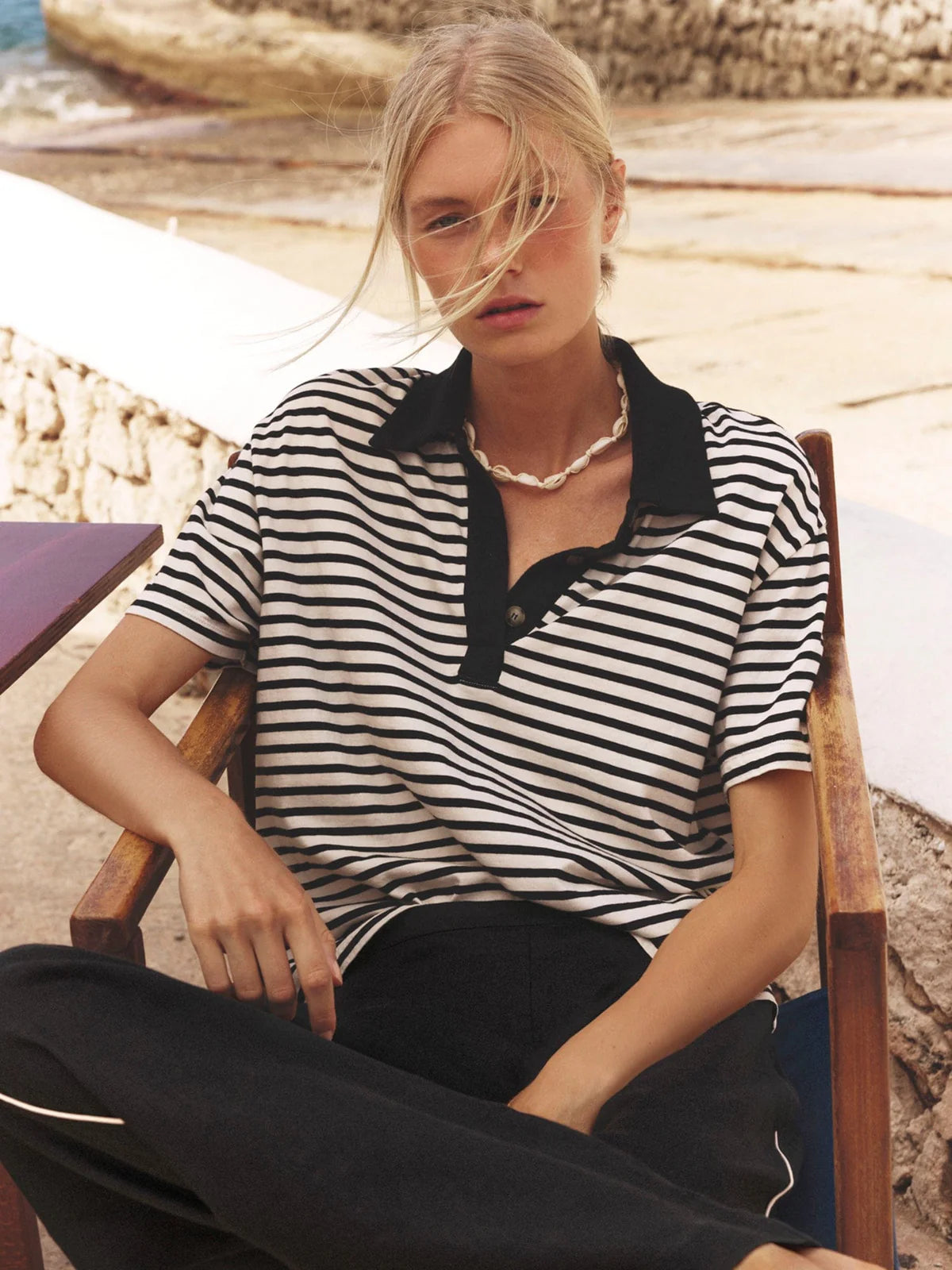 Woman wearing a black and white striped shirt sitting outdoors near water.