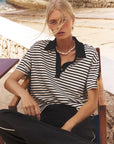 Woman wearing a black and white striped shirt sitting outdoors near water.