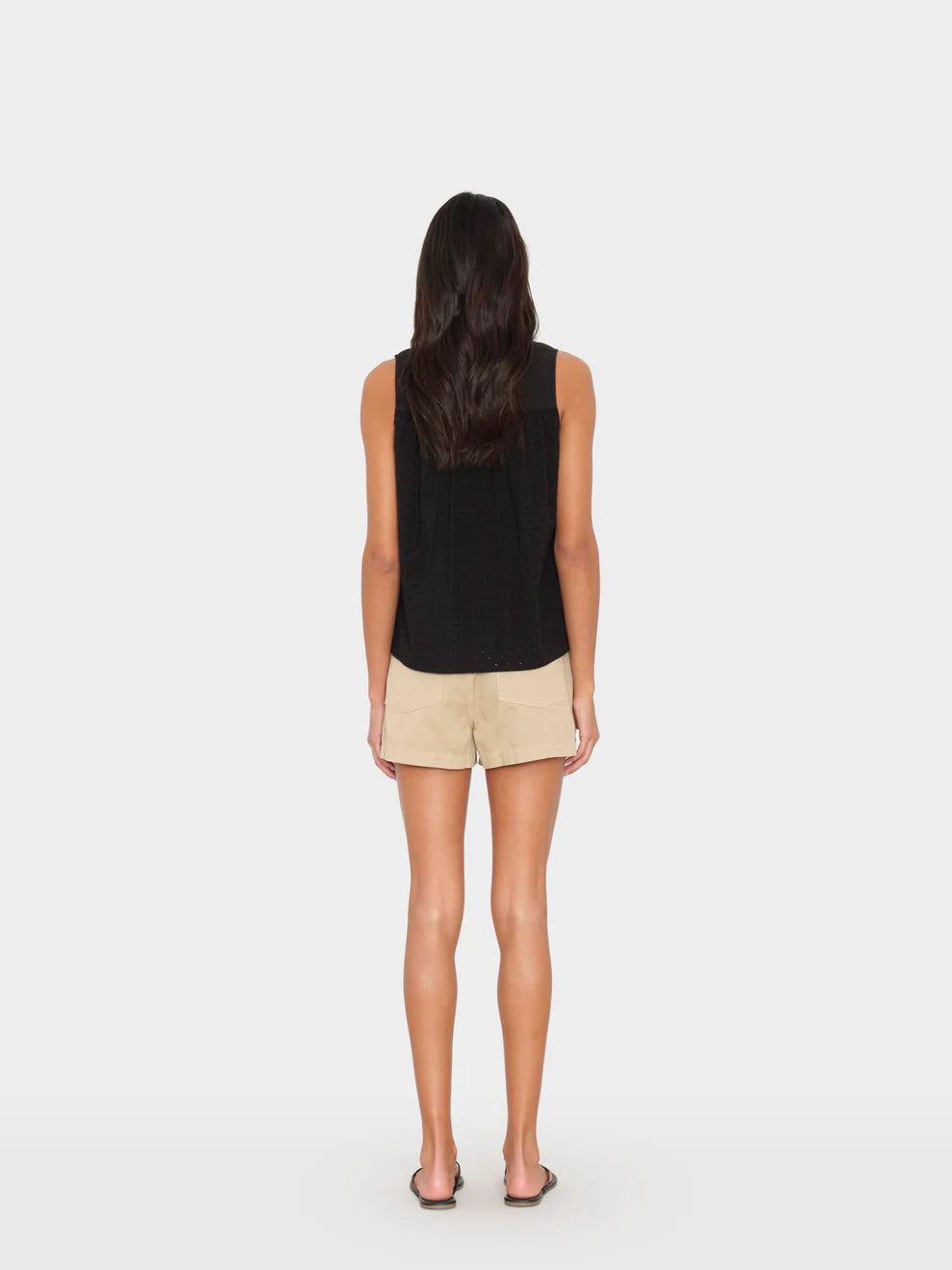 Woman wearing a black sleeveless top and beige shorts on a white background