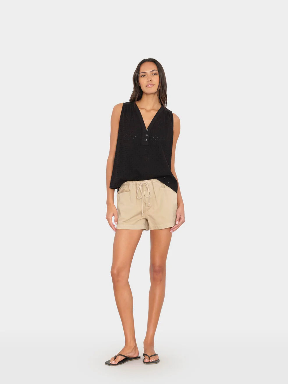 Woman wearing a black sleeveless top and beige shorts on a white background
