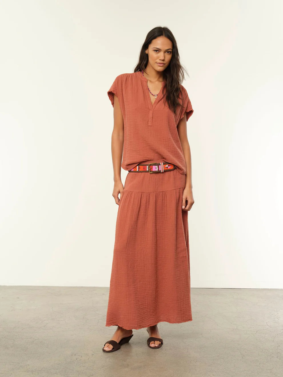 Woman wearing a rust-colored outfit with a belt against a white background