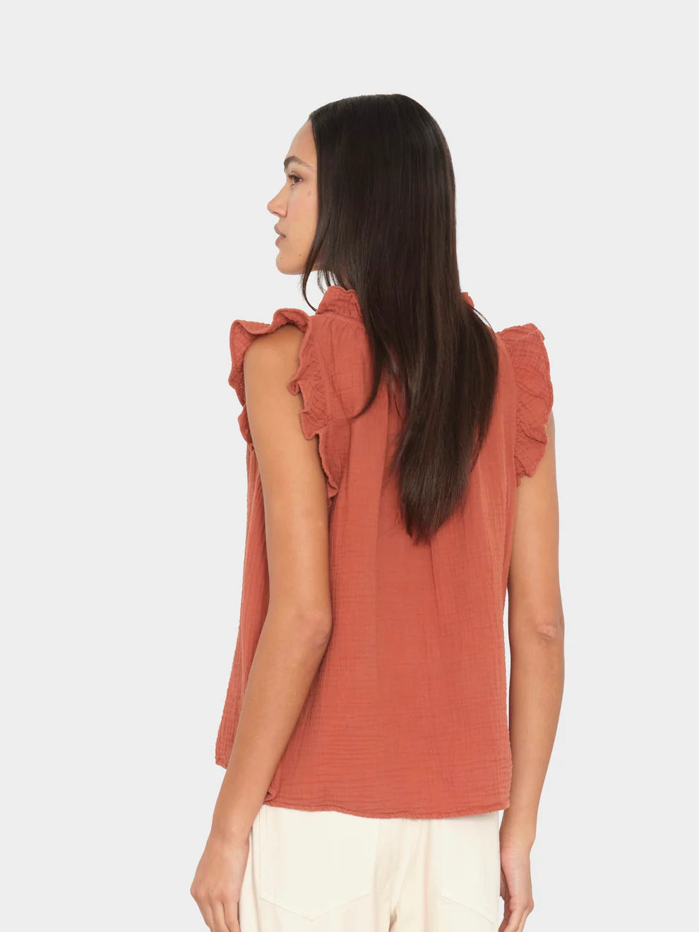 Woman wearing a rust-colored sleeveless top with ruffled shoulders on a white background