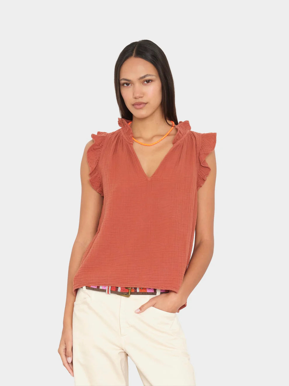 Woman wearing a rust-colored sleeveless top with ruffled shoulders on a light gray background