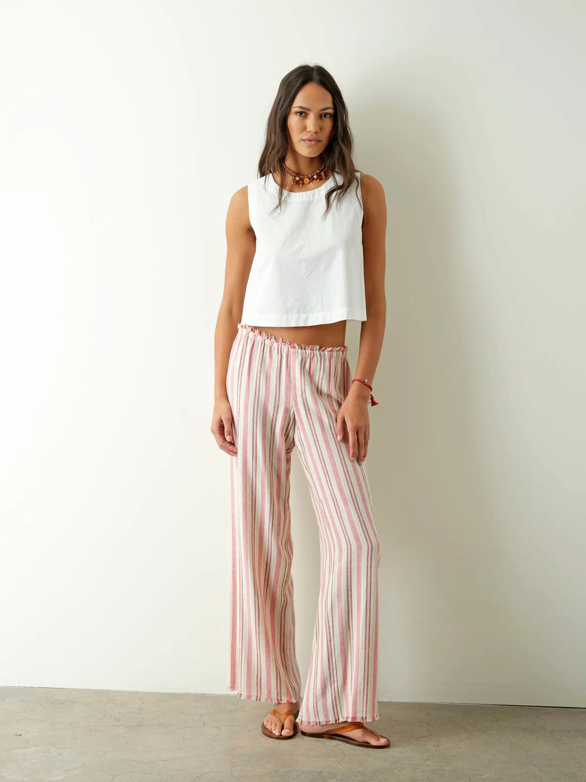 Woman wearing a white sleeveless top and pink striped pants against a plain background
