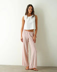 Woman wearing a white sleeveless top and pink striped pants against a plain background