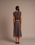 A woman viewed from the back wearing a sleeveless ruffled top and midi skirt set with a small-scale geometric pattern in dark purple and orange, set against a plain taupe studio background.