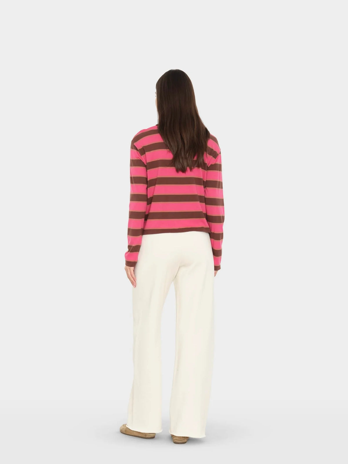 model wearing a pink and brown stripe sweater with wide leg cream sweatpants on a white background , back view