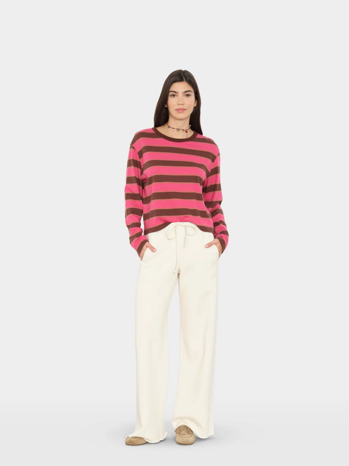 model wearing a pink and brown stripe sweater with wide leg cream sweatpants on a white background 
