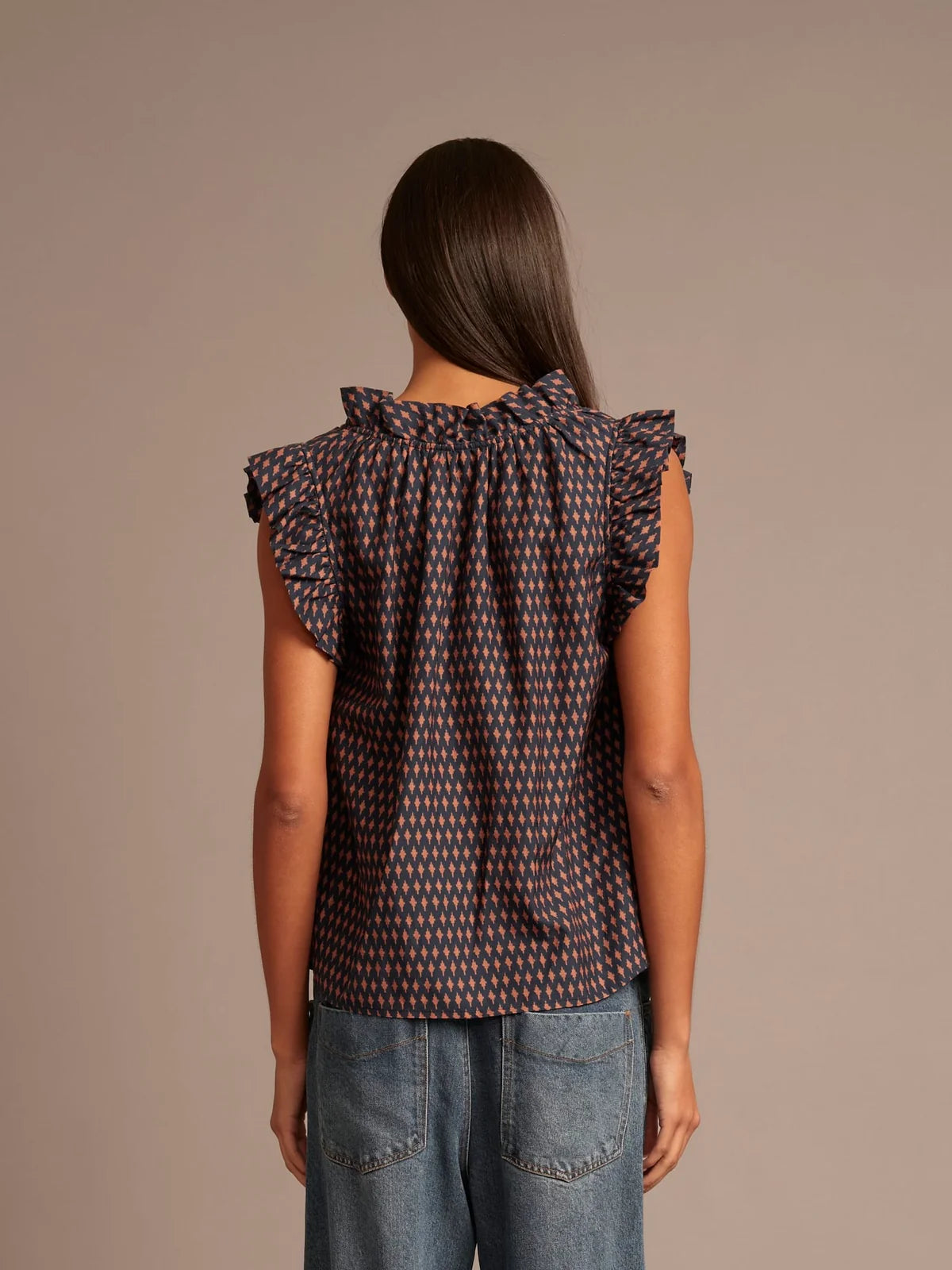 Woman wearing a patterned top and jeans against a brown background