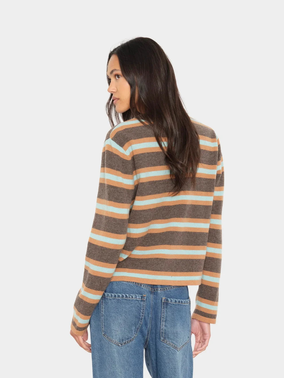 A woman shown from the back wearing a cropped, long-sleeve knit sweater with horizontal stripes in brown, beige, and light blue, paired with blue jeans, against a light gray studio background.