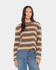 A woman modeling a long-sleeve knit sweater with horizontal stripes in brown, beige, and light blue, paired with blue jeans, against a light gray studio background.