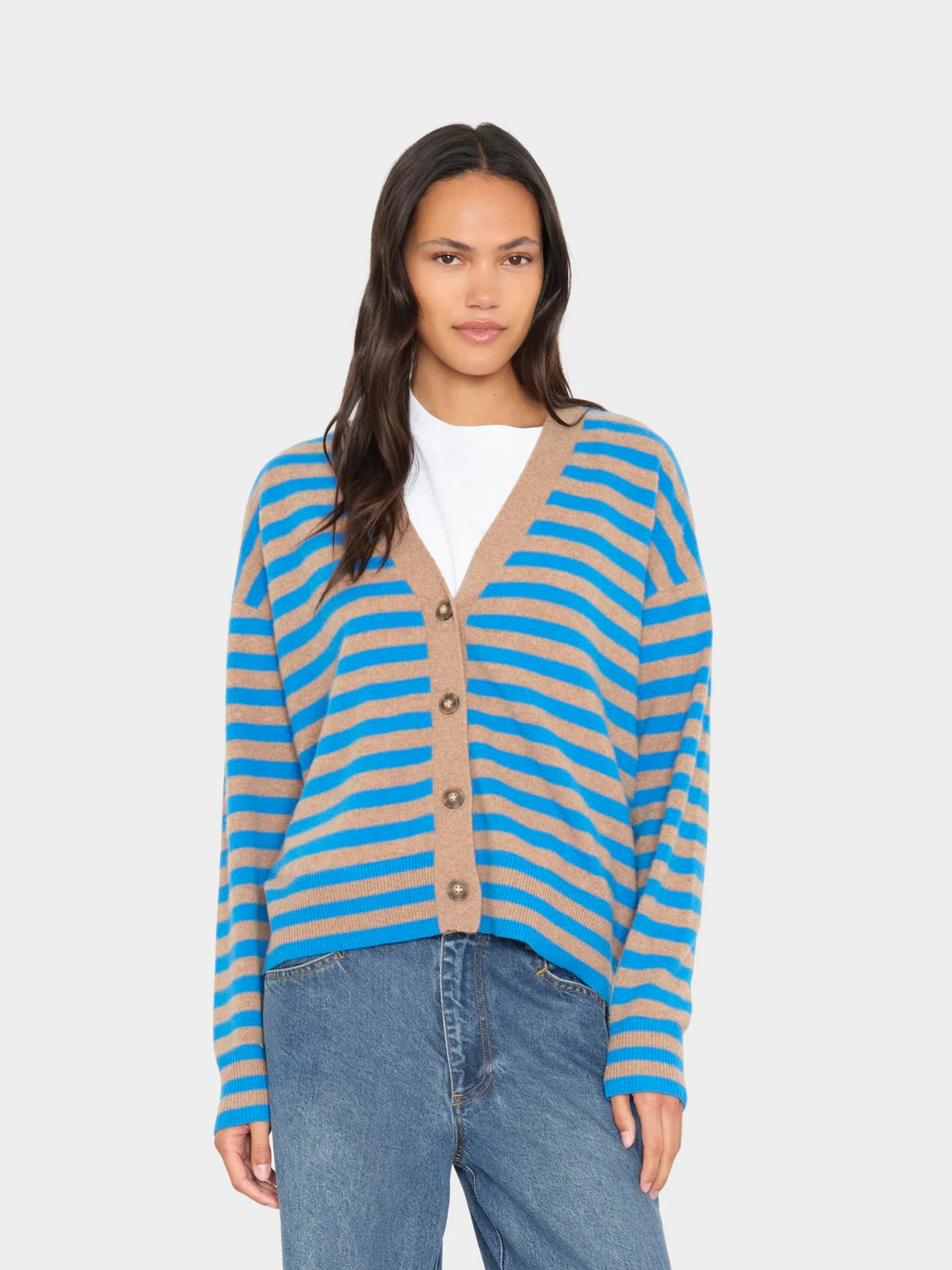 model wearing a tan and blue stripe vneck button down cardigan over a white top with blue jeans on a white background 