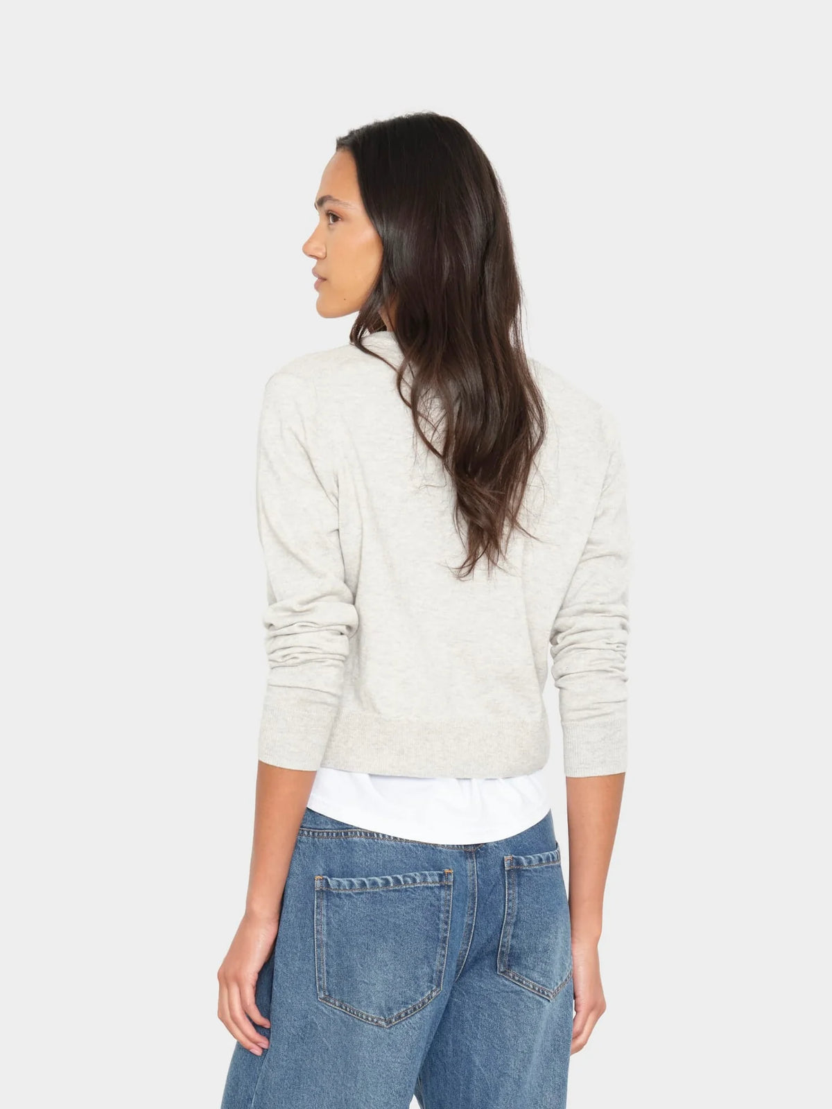 model wearing a grey cardigan over a white top with jeans on a white background, back view 