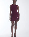 A woman modeling a sleeveless, deep burgundy wrap-style mini dress with a tie waist and decorative gold-tone buttons on the side, paired with black strappy high-heeled sandals against a plain white studio background.