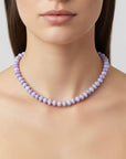 Woman wearing a purple beaded necklace against a neutral background
